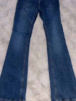 Blå bootcut jeans med utsvängda ben - Säljer ett par klassiska blå bootcut jeans med utsvängda ben och snygga sömmar. Jeansen har fem fickor och normal midja. Perfekta för dig som gillar retrostil och vill ha ett par jeans som sticker ut lite extra.