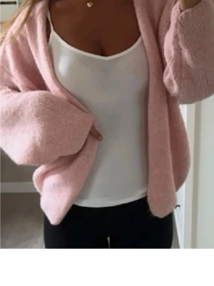 Ljusrosa oversized stickad kofta - Mysig ljusrosa stickad kofta med oversized passform och vida ärmar. Perfekt att slänga över en topp för en avslappnad look. Koftan är öppen framtill och har en fluffig känsla. Passar dig som gillar en chill och trendig stil.