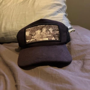 Sällsynt maggiore keps - Svart truckerkeps med mesh baktill och justerbar rem. Framtill finns ett stort vintageinspirerat foto i svartvitt som motiv. Kepsen har böjd skärm och klassisk passform.Från Maggiore exlusiv model dust bag kommer med