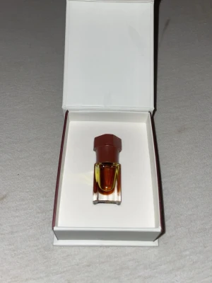 Mukhalat Nagdy Malaky parfymolja - Exklusiv parfymolja i en liten glasflaska med brun kork, levereras i en elegant vit ask med bruna detaljer. Oljan har en djup bärnstensfärg och flaskan har en modern, kantig design. Perfekt för dig som gillar orientaliska dofter.