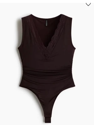 Mörkbrun body med spetsdetalj - Snygg mörkbrun body med djup V-ringning och spetskant. Ärmlös modell i mjukt stretchigt material som sitter figurnära och har rynkade detaljer i midjan. Perfekt för en trendig och stilren look.