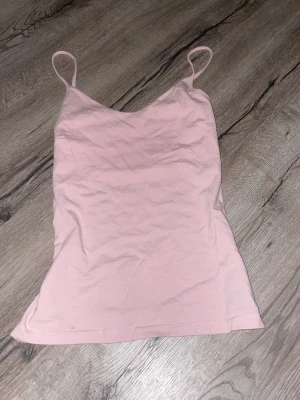 Ljusrosa linnetopp med tunna band - Söt ljusrosa linnetopp med tunna axelband och enkel, stilren design. Toppen har en mjuk och följsam passform som gör den perfekt till många olika outfits. Materialet känns lätt och bekvämt mot huden.