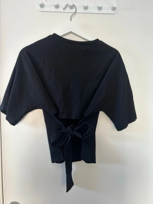 Svart topp med knyt från Nelly - Svart topp från Nelly med korta ärmar och öppen rygg. 🥰🥰❤️💞🩷