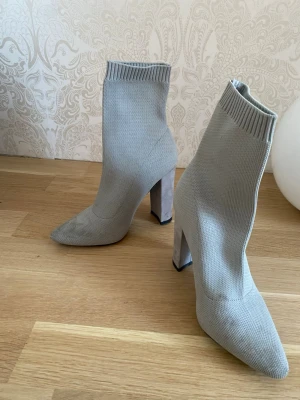 Grågröna stövletter 35 - Snygga grågröna stövletter i stickat material med spetsig tå och bred hög klack. De har en ribbad kant upptill som ger en cool sockboots-look. Smuts förekommer framme vid tån. Stolek 2 som motsvarar 35.