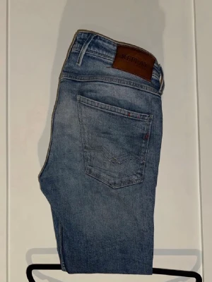 Replay Anbass - Snygga blå jeans från Replay med klassisk femficksdesign och läderpatch med logga bak i midjan. Jeansen har en rak passform och diskreta slitningar för en avslappnad look. Perfekta till vardags och passar till det mesta.