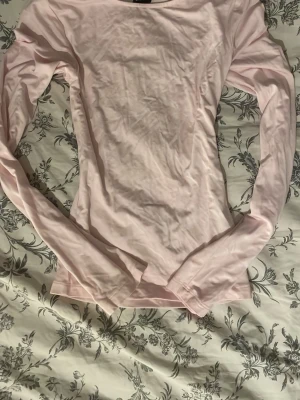 Ljusrosa långärmad topp - En enkel och stilren ljusrosa långärmad topp i mjuk bomull. Modellen har en klassisk rund halsringning och en slim passform som sitter snyggt på kroppen. Perfekt att matcha med jeans eller kjol för en clean look.