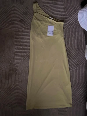 Grön  one shoulder klänning Filippa K  - Snygg grön one shoulder klänning från Filippa K. Klänningen har en enkel och stilren design med axelbandslös skärning på ena sidan. Tillverkad i mjukt material som ger en bekväm passform. Perfekt för dig som gillar minimalistisk stil.