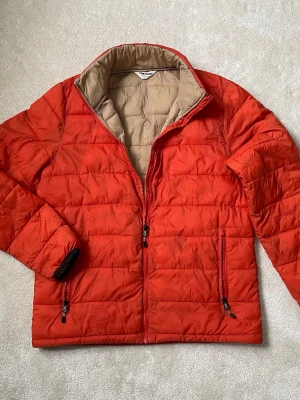 Tretorn dunjacka / vårjacka  - Snygg orange vårjacka från Tretorn med beige insida och svarta detaljer vid ärmslut. Jackan har två dragkedjeförsedda fickor framtill och quiltad design. Perfekt för krispiga våren 