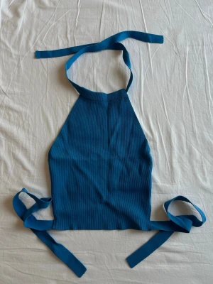 Blå ribbad halterneck linnetopp - Säljer en blå ribbad linnetopp med halterneck och långa knytband i nacken och midjan. Sparsamt använd, i gott skick!