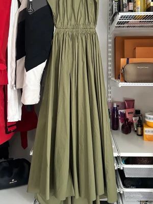 Michael Kors klänning - Snygg olivgrön långklänning med markerad resår i midjan och vid axlarna. Klänningen har en luftig och voluminös kjol som ger en cool och avslappnad vibe. Perfekt för dig som gillar stilrena och trendiga plagg med enkel design.