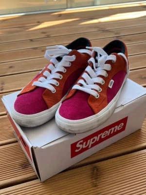 Vans x Supreme rosa/orange sneakers - Unika Vans x Supreme sneakers i samarbete, med rosa manchestertyg och orange mockadetaljer. Klassisk låg modell med vita snören och sula. Perfekta för dig som vill sticka ut med färg och stil. Vans-logga på sidan och Supreme-boxen medföljer.