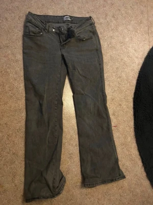 Grå bootcut jeans med broderade fickor - Säljer ett par grå bootcut jeans med snygga broderade detaljer på bakfickorna. Jeansen har klassisk femficksdesign, låg midja och är tillverkade i denim. Perfekta för dig som gillar en avslappnad men ändå trendig stil.