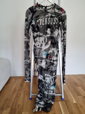 Långärmad bodycon meshklänning från Versace - Cool långklänning från Versus/verscei meshmaterial med svartvitt grafiskt mönster och tryck. Klänningen har lång ärm, rund halsringning och figurnära passform. Perfekt för dig som vill sticka ut med en edgy streetstyle-look.