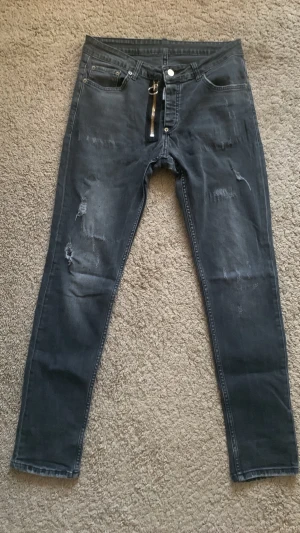 Dsquared2  - Säljer ett par DSQ2 mörkgrå/svarta slim jeans med slitna detaljer och en snygg dragkedja framtill. Jeansen har fem fickor, låg midja och smal passform. Materialet är stretchigt denim som ger en tajt och bekväm känsla. Perfekt för dig som gillar en trendig och avslappnad stil. Kan ändra priset 
