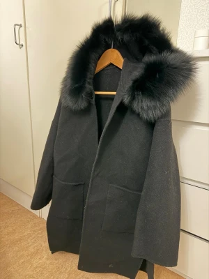 Svart kappa med päls luva - Använd 2 gånger.   Varm, bekväm och stilren – passar vinter vår och höst. Hör gärna av dig om du vill ha mått eller fler bilder 