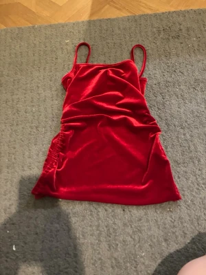 Röd sammetsklänning med smala band - Snygg röd kortklänning i mjuk sammet med smala axelband och lätt rynkade detaljer på sidan. Perfekt för dig som vill sticka ut med en färgstark och trendig look.