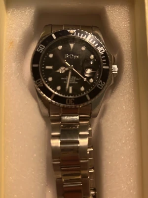 Submarine klocka - Stilren klocka  med silverfärgad länk i metall och svart urtavla. Klockan har tydliga vita markeringar, datumfönster och vridbar bezel. Perfekt accessoar för dig som gillar klassisk och tidlös design.