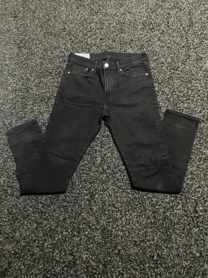 Svarta skinny jeans med fem fickor - Säljer ett par svarta skinny jeans med klassisk femficksdesign och silverfärgade nitar. Jeansen har smal passform och normal midja. Perfekta till en avslappnad streetstyle-look. Materialet känns stretchigt och bekvämt.