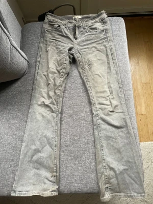 Grå bootcut jeans - Snygga grå jeans med bootcut passform och klassiska fem fickor. Jeansen har en tvättad look och stängs med dragkedja och knapp. Perfekta för en avslappnad och trendig stil.