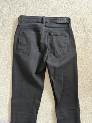 Svarta skinny jeans från Lee - Säljer ett par svarta skinny jeans från Lee med klassisk femficksdesign och smal passform. Jeansen har bälteshällor och Lee-logga på bakfickan. Perfekta för dig som gillar en stilren och enkel look. Storlek: W28L31
