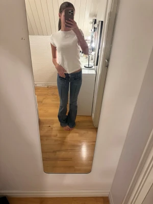 Blå bootcut jeans med låg midja - Snygga blå bootcut jeans med låg midja och klassiska fickor fram och bak. Jeansen har ljusa slitningar och kontrastsömmar som ger en cool vintagekänsla. 