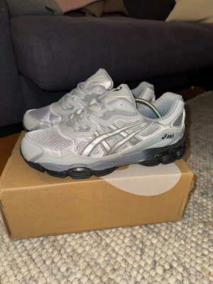 Asics Gel NYC - Snygga sneakers från Asics i grått med silvriga detaljer och svart chunky sula. Skorna har meshpaneler för extra ventilation och klassisk Asics-logga på sidan. Perfekta för dig som gillar sportig och clean stil.