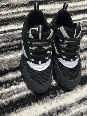 Svarta och grå Dior sneakers - Snygga sneakers från Dior i svart och grått med vita detaljer. Skorna har meshpaneler för extra andningsförmåga och reflekterande detaljer. Klassisk låg modell med snörning och robust sula. Perfekta för dig som vill ha en stilren och modern look.