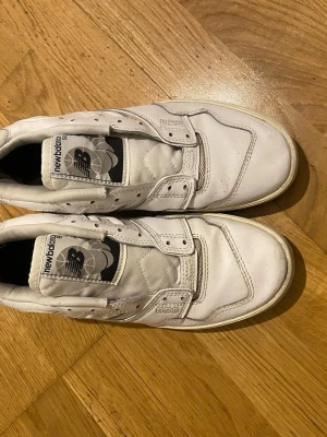 Vita New Balance 550 sneakers - Snygga vita New Balance 550 sneakers med klassisk siluett och svart logga på plösen. Skorna har en mix av läder och mesh för både stil och komfort. Perfekta för dig som gillar retrovibbar och streetwear.