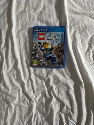 LEGO City Undercover till PS4 - LEGO City Undercover till PlayStation 4. Spelet har ett blått fodral och framsidan visar en LEGO-polisfigur i action. Omslaget har färgglada illustrationer och spelet är märkt med PEGI 7. Perfekt för dig som gillar äventyr och humor i LEGO-världen.