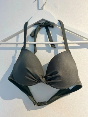 Mörkgrön bikiniöverdel med knyt - Snygg mörkgrön bikiniöverdel med vadderade kupor och twistad detalj framtill. Knyt i nacken och justerbart spänne i ryggen för perfekt passform. Storlek 75B. Använd endast någon gång. 