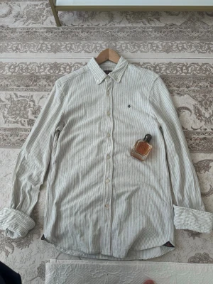 Randig skjorta från Morris - Snygg vit skjorta med tunna grå ränder från Morris beige och vit . Klassisk krage, knappar framtill och långärmad modell. Ny pris 1699 och mitt pris 299✨⭐️, Tillverkad i mjuk bomull som känns skön mot huden. Perfekt för dig som gillar stilrena och tidlösa plagg, vid minsta funderingar eller om ni vill ha mer bilder så är det bara säga till 🙂