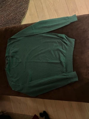 Grön V-ringad tröja Massimo Dutti - Mörkgrön tunnstickad tröja från Massimo Dutti med V-ringning och ribbade muddar. Tröjan är i mjuk ull och cashmere-blandning, perfekt för dig som gillar stilrena och klassiska plagg. Passar lika bra till jeans som till chinos.