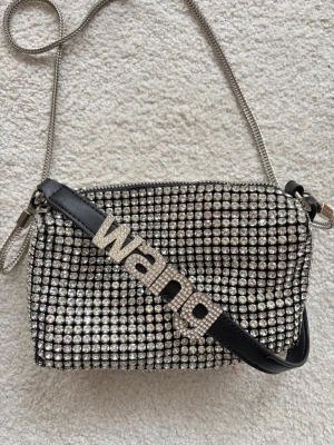 Glittrig handväska från Alexander Wang - Säljer en glittrig handväska från Alexander Wang med silverfärgade strass över hela väskan och en metallkedja som axelrem. Väskan har en svart läderdetalj med 'wang' i stora bokstäver i strass. Perfekt för dig som vill sticka ut.