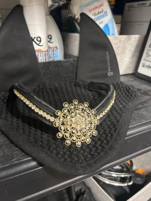 Pannband  - Snyggt svart pannband till häst med en guldig kristall med svart. En fin detalj när man vill se snygg ut på tävling, perfekt med huva under. Perfekt för dig som vill sticka ut på ridbanan och matcha med resten av outfiten! Pannbandet är från Divoyh och modellen heter ”Ysanne” och har storleken COB.