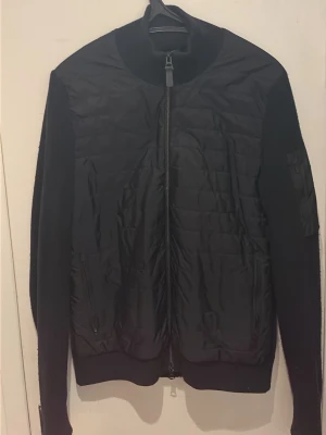 Svart cardigan från J.Lindeberg - Säljer nu min absoluta favoritjacka då den har blivit för liten! Den har en quiltad framsida och stickade ärmar/baksida och är perfekt nu till våren över tshirt eller tjocktröja/hoodie. Den är i storlek S men passar även M. Inga märkbara defekter förutom visst slitage på J.lindeberg märket på ärmen. Nypris 3200kr. Mitt pris 999kr! Hör av er vid frågor eller om ni vill ha fler bilder!