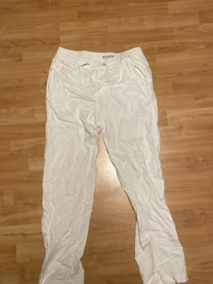 Vita linnebyxor med dragsko - Säljer ett par vita linnebyxor från C i en skön linne/viskosblandning. Byxorna har resårmidja med dragsko och raka ben för en avslappnad look. Perfekta för varma dagar och enkel att matcha med olika toppar.