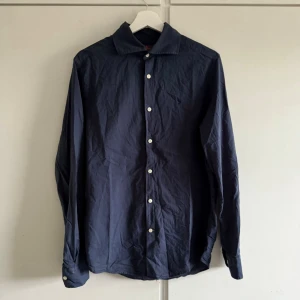 Mörkblå Morris skjorta  - Stilren mörkblå morris skjorta med klassisk krage och vita knappar framtill. Skjortan har lång ärm och är tillverkad i ett mjukt bomullstyg. Perfekt för en clean och enkel look. Lite urtvöttad därav priset