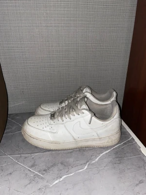 Vita Nike Air Force 1 sneakers - Klassiska vita Nike Air Force 1 sneakers med lågt skaft. Skorna har perforerad tå, vita skosnören och den ikoniska swoosh-loggan på sidan. Tillverkade i läder med gummisula för bra .SKORNA RENGÖRS INNAN DU FÅR DE