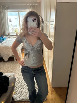 Ljusblå omlottblus i satin! - Söt ljusblå omlottblus/festtopp med v-ringning och en rosett/knyte i sidan. Den kan se silvrig ut på bilderna men den är ljusblå!🩵 Står inget märke men den är köpt secondhand på humana!