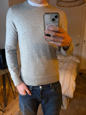 Ljusgrå basic tröja i bomull - En stilren ljusgrå tröja med rund halsringning och långa ärmar. Tröjan är tillverkad i mjuk bomull och har ribbade muddar vid ärmslut och nederkant. Perfekt för en clean och enkel look.