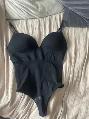 Svart body med vadderade kupor - Snygg svart body med justerbara axelband och vadderade kupor. Bodyn har en bra passform och är stretchig. Från HM.