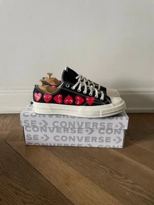 Converse x CDG Play svarta sneakers - Snygga Converse x Comme des Garçons Play sneakers i svart canvas med vita sulor och snören. På sidan finns de ikoniska röda hjärtana med ögon. Klassisk låg modell som passar till det mesta och har en cool streetwear-vibe. Storlek 42, helt nya.