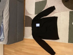 Svart hoodie från Casablanca - Säljer en svart hoodie från Casablanca med stor grafisk print i blått och vitt på ryggen där det står 'Casa Blanca'. Hoodien har huva och en mindre matchande print på bröstet. Perfekt för dig som gillar streetwear och vill sticka ut.