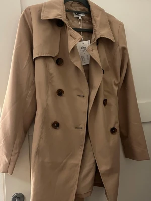 Trenchcoat  - Beige brun trenchcoat i storlek S. Aldrig använd med prislapp. Köpt för 699 säljer för 499.