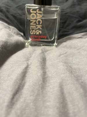 Jack & Jones Everyday Boost parfym - Fräsch parfym från Jack & Jones i modellen Everyday Boost. Flaskan är genomskinlig och fyrkantig med svart lock och tydlig logga i vitt och rött på framsidan. Perfekt för dig som vill ha en enkel och stilren doft i badrumsskåpet.