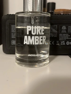 PURE AMBER parfym från Jack & Jones - Fräsch parfym från Jack & Jones med namnet PURE AMBER. Flaskan är cylindrisk i genomskinligt glas med silverfärgad spraykork och tydlig vit text på framsidan. Doften har en modern och stilren känsla, perfekt för dig som gillar minimalistisk design.