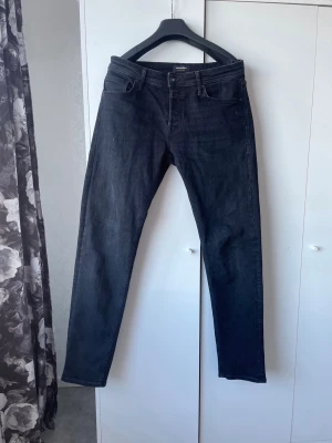 Svarta raka jeans från Jack & Jones - Mörka svarta jeans från Jack & Jones med klassisk femficksdesign och raka ben. Jeansen har normal midja. En clean och enkel modell som funkar till det mesta.