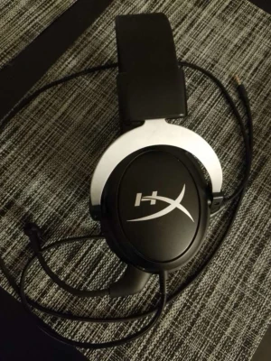 HyperX gaming headset med mikrofon - Säljer ett par svarta over-ear HyperX hörlurar med inbyggd mikrofon och kabelanslutning. Hörlurarna har mjuka, vadderade kåpor och justerbart huvudband i konstläder samt detaljer i metall. Perfekta för gaming och långa sessions vid datorn.