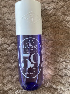 Sol de Janeiro Cheirosa 59 Perfume Mist - Sol de Janeiro Cheirosa 59 Perfume Mist i en snygg lila plastflaska med vit kork. Flaskan har en modern, rundad form och tydlig logga framtill. Perfekt för dig som gillar fräscha och unika dofter med en tropisk vibe. Den är använd. Se på bild hur mycket som har användts! Ca 200 ml kvar