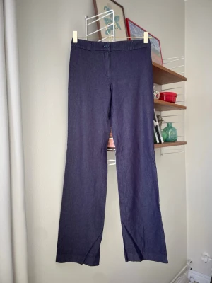Lågmidjade byxor  - Byxor med låg midja i denimliknande mjukt tyg med stretch (materialförteckning har klippts bort). Strl 36. Midjemått: 67 cm, innerbenslängd: 75 cm. Färgen är indigoblå och skiftar lite beroende på ljus (se bilder). Lite slitet längst ned på byxbenen, i övrigt fint skick!
